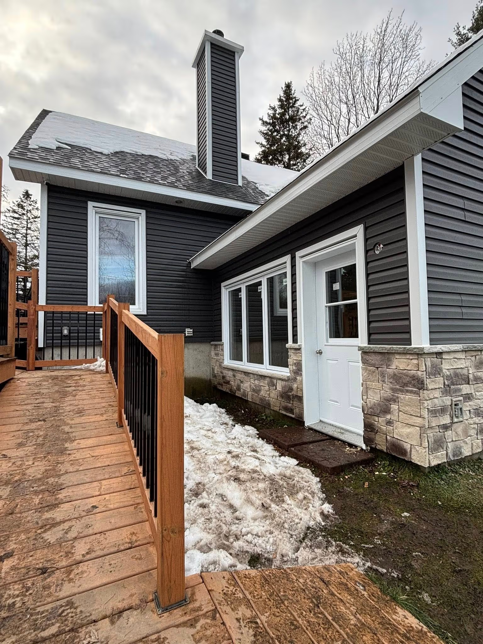 Renovated home facade with black exterior siding, decorative stone, white windows and wood ramp