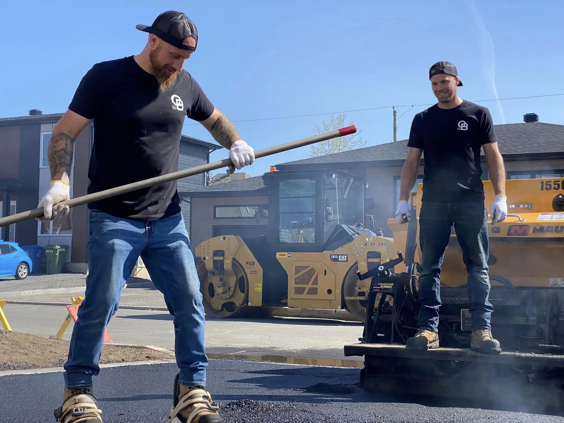 Workers laying hot asphalt using paver machine and compactor on residential driveway