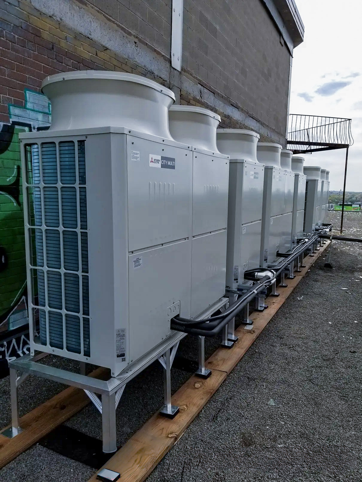 Climatisation commerciale Mitsubishi installée sur le toit d’un bâtiment, montrant plusieurs unités extérieures alignées et connectées par des conduits et câbles techniques.