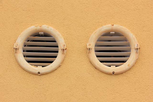 Two round ventilation outlets with horizontal grilles on a textured yellow stucco exterior wall.