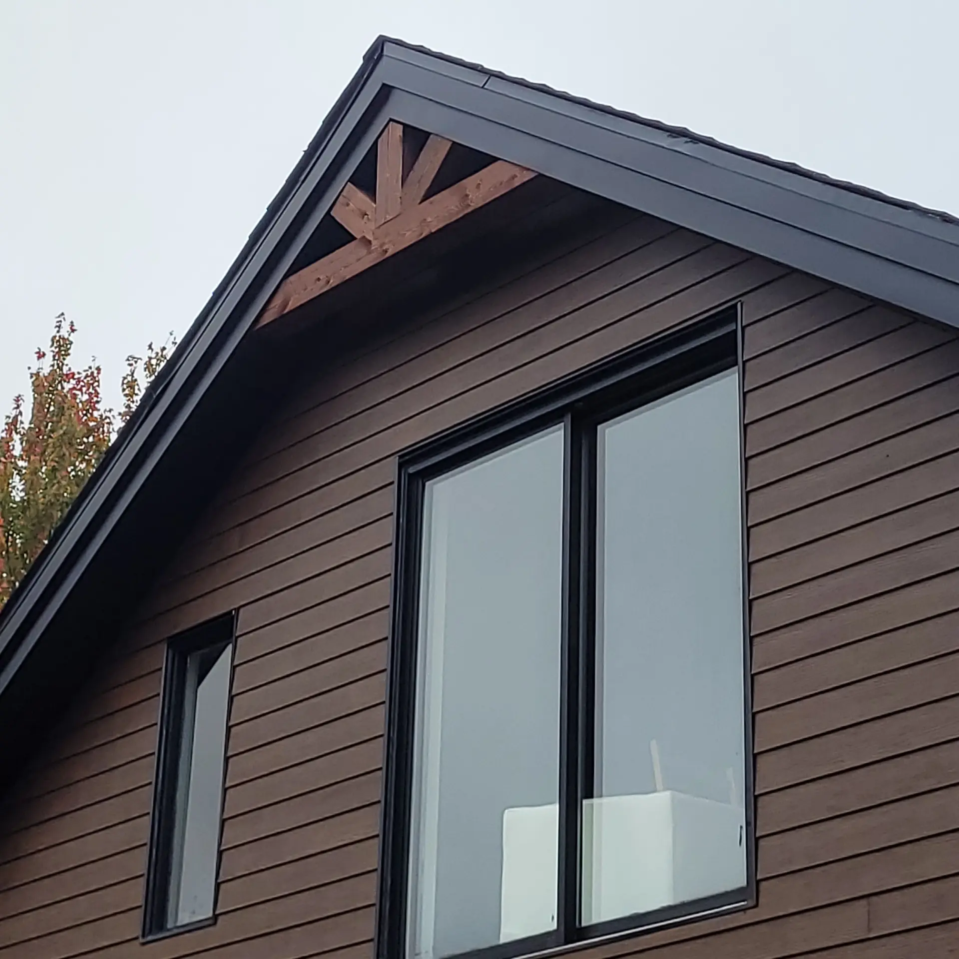 Façade moderne avec revêtement en bois, grandes fenêtres et charpente apparente.