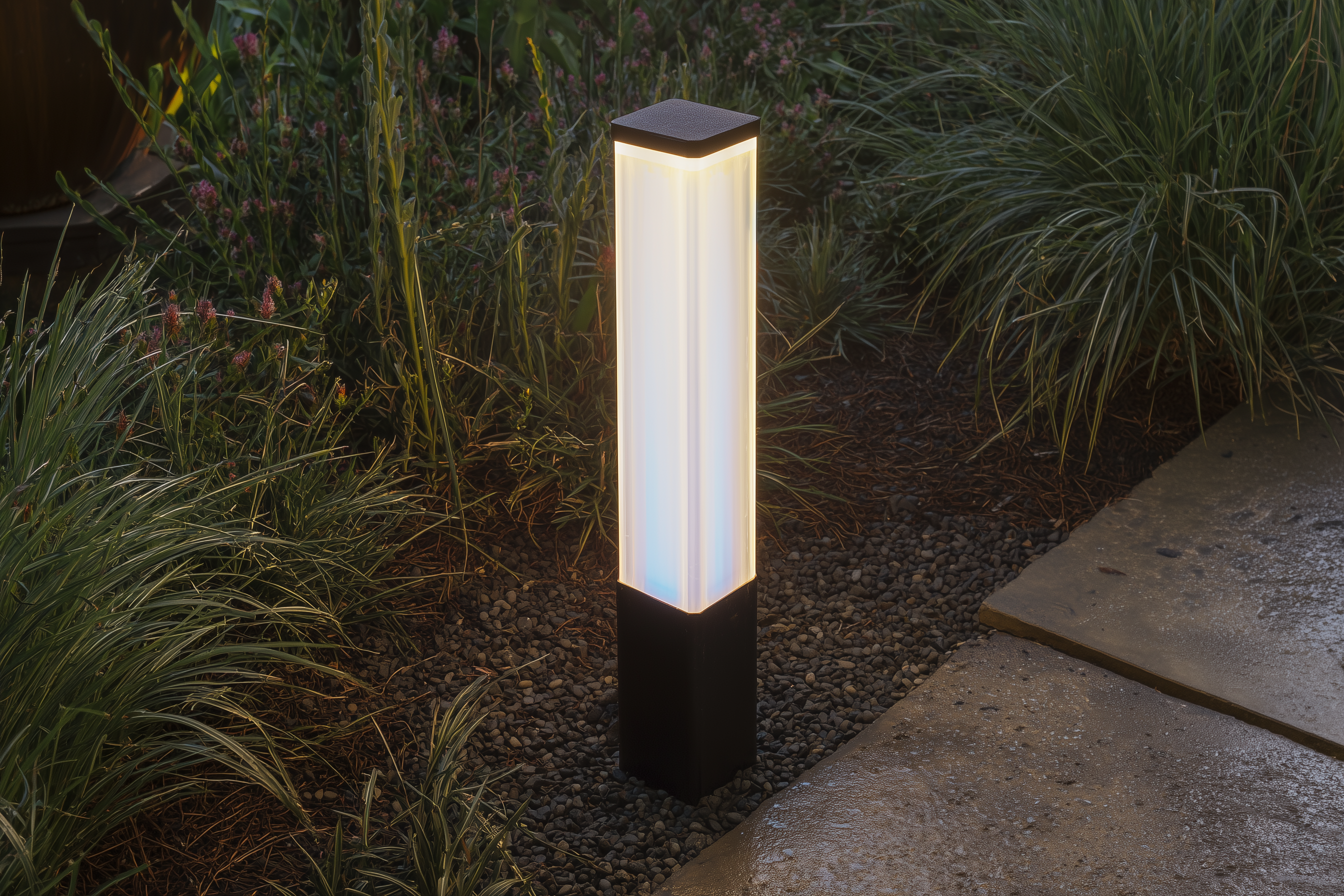 Modern light bollard illuminating a garden path surrounded by vegetation