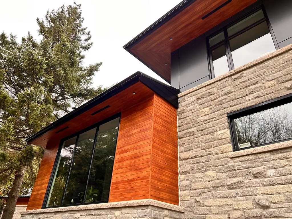 Contemporary house with natural wood siding, grey stone veneer, black panels, large windows, and wood soffits