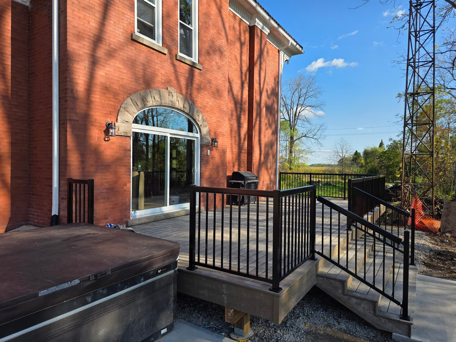 Outdoor wooden deck with black metal railings, hot tub and red brick facade with large glass door
