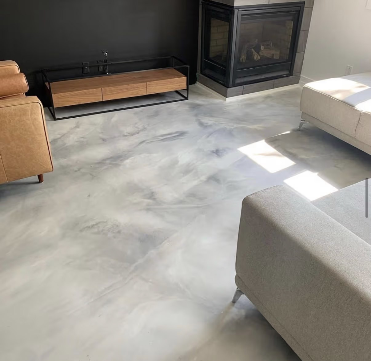 Modern living room with light gray marbled epoxy flooring, glass fireplace, black wall, wood cabinet and light sofa.