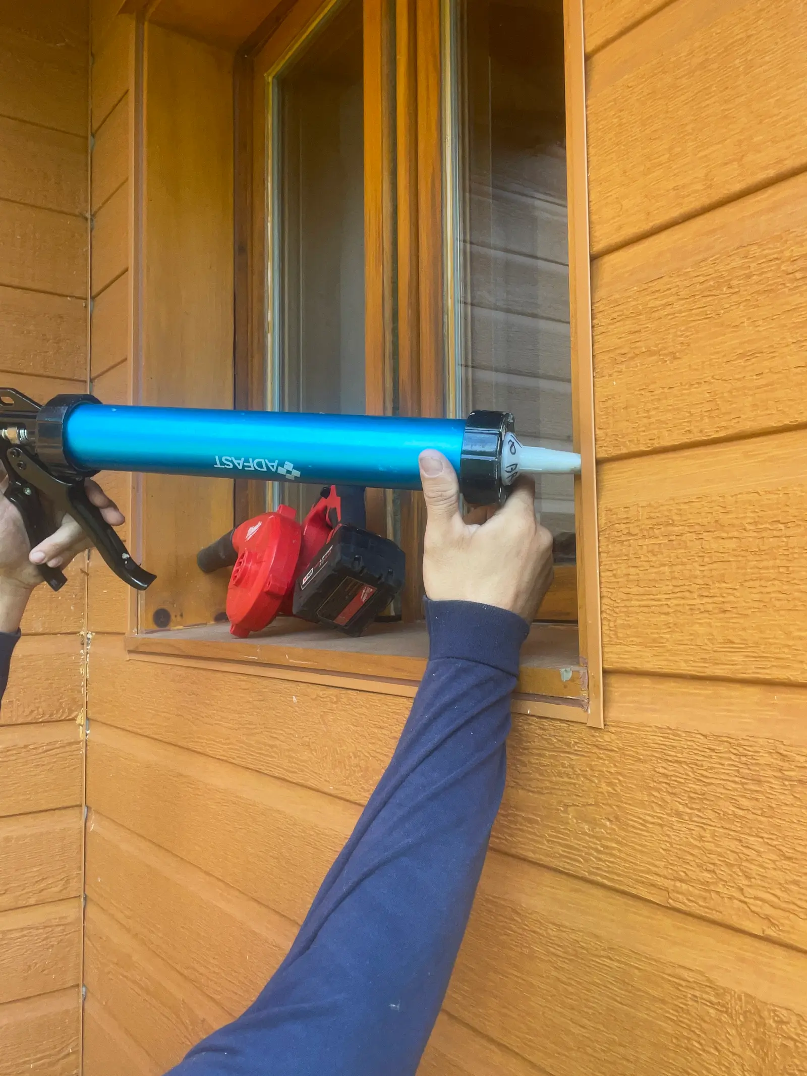 Calfeutrage extérieur d’une fenêtre en bois avec pistolet à scellant sur revêtement orange