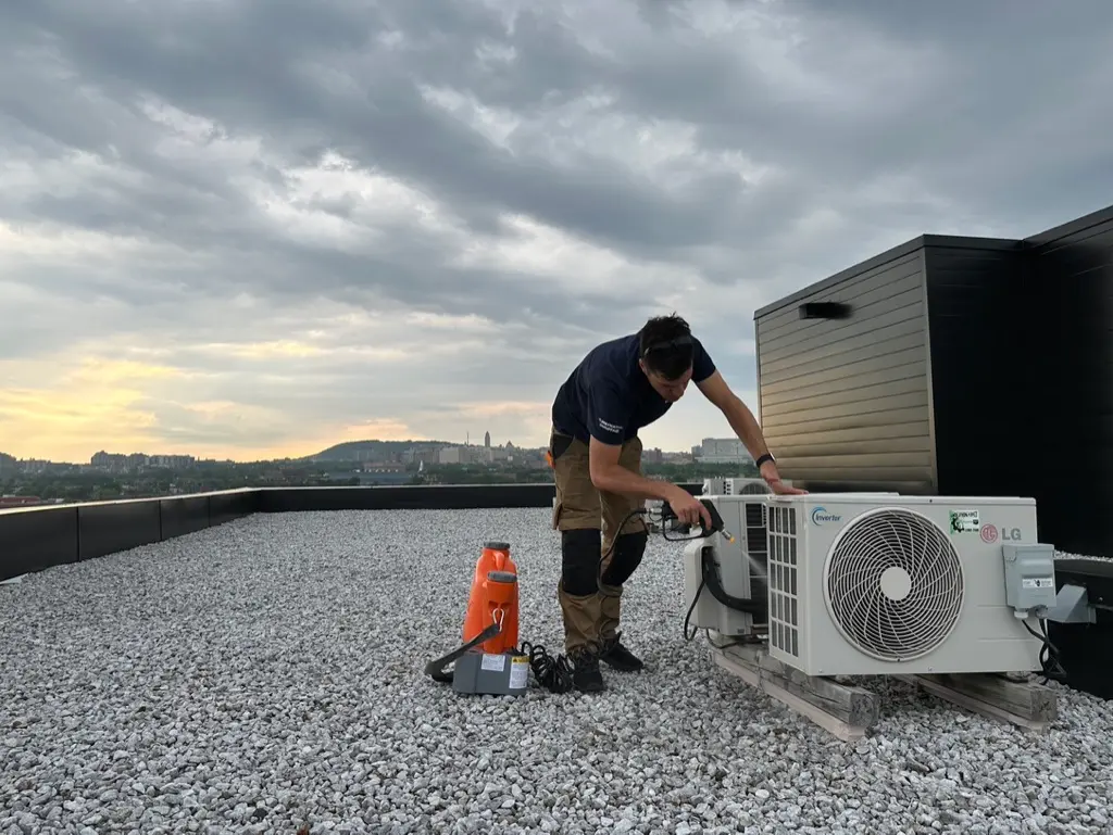 Technician installing an outdoor air conditioning unit on a flat roof with an urban view.