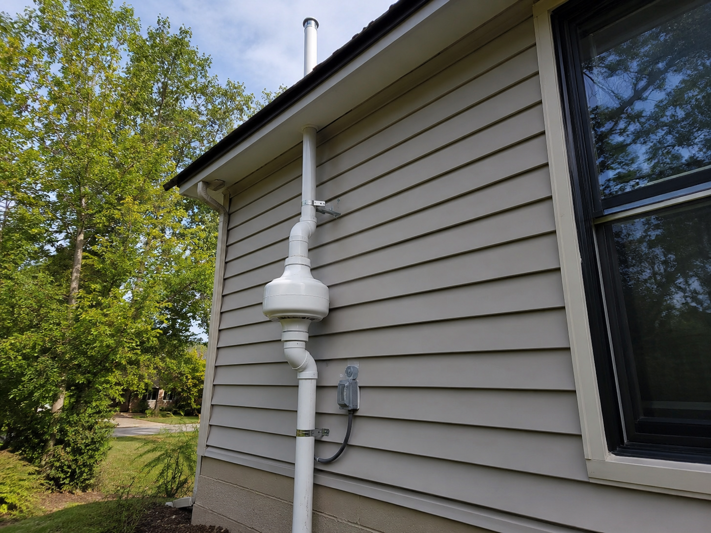 Exterior radon mitigation system mounted on a house wall.