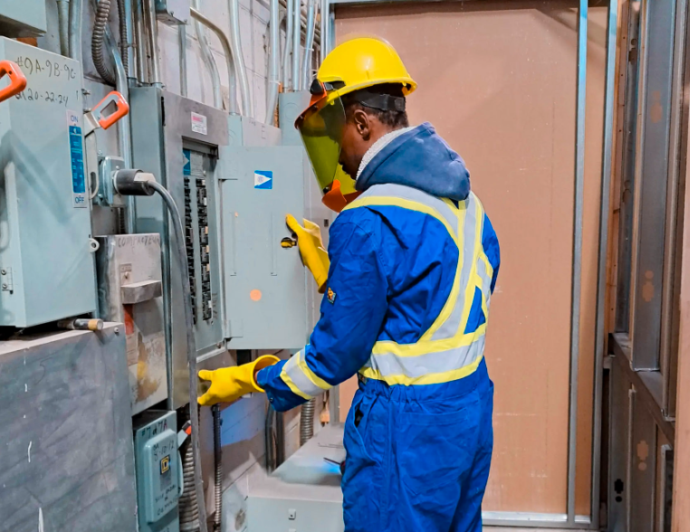 Electrician in safety gear handling an electrical panel in an industrial building
