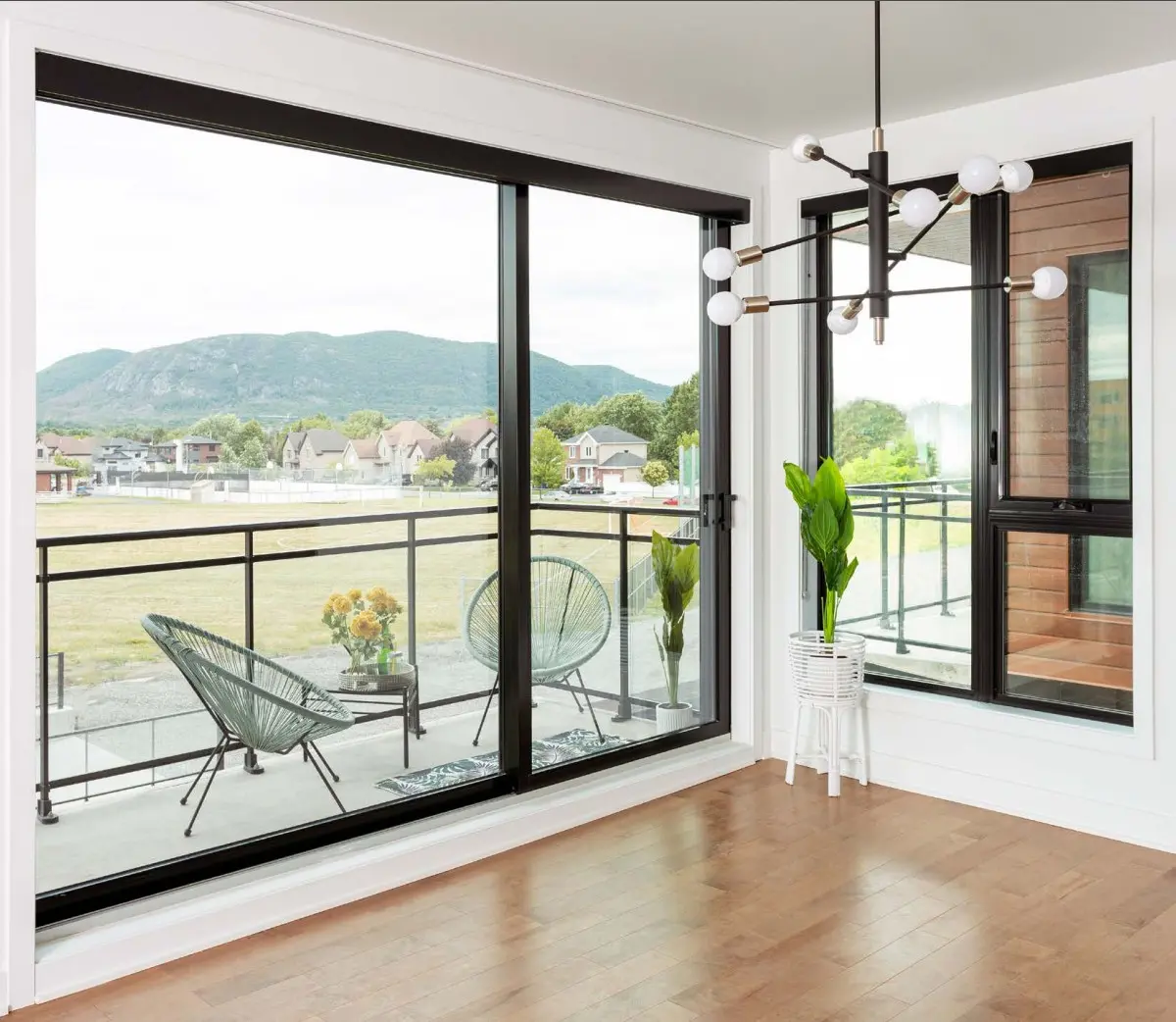 Portes-fenêtres coulissantes modernes offrant une vue panoramique sur un balcon avec mobilier et montagnes en arrière-plan.
