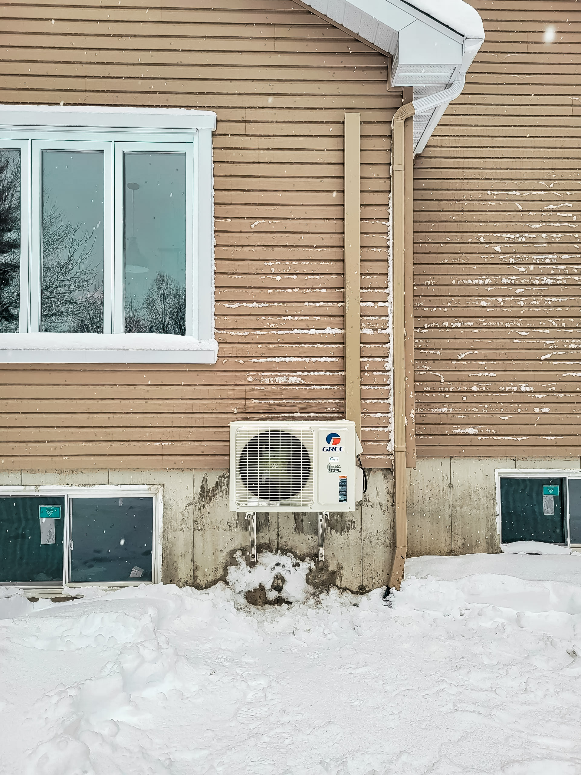 Unité extérieure de climatisation GREE installée sur le mur d'une maison résidentielle en hiver.