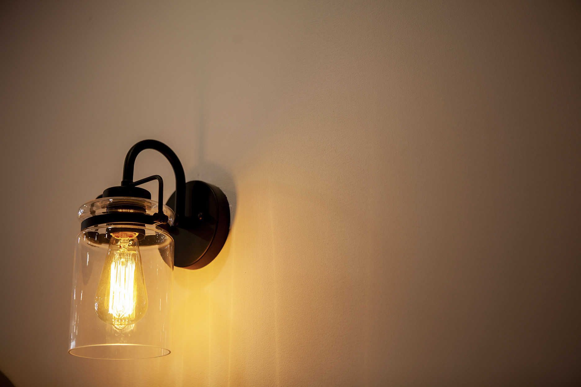 Black wall light with lit Edison bulb and clear glass shade diffusing a warm light