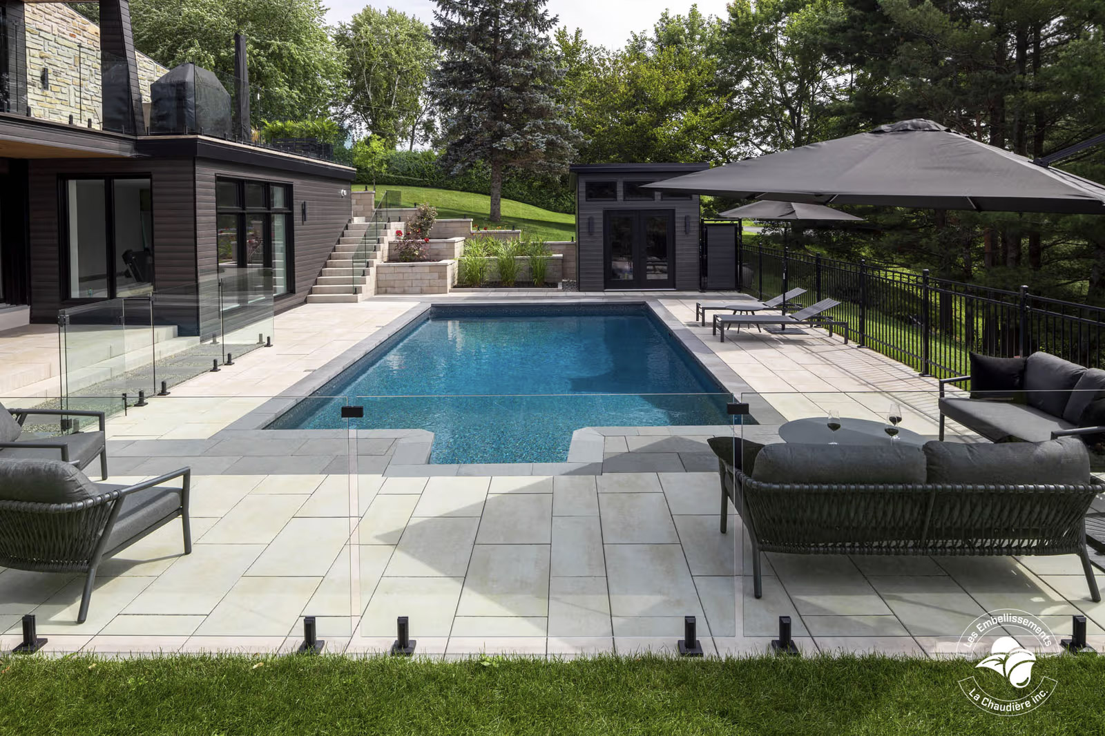 Modern backyard with in-ground pool, glass fence, paving, patio and high-end landscaping.