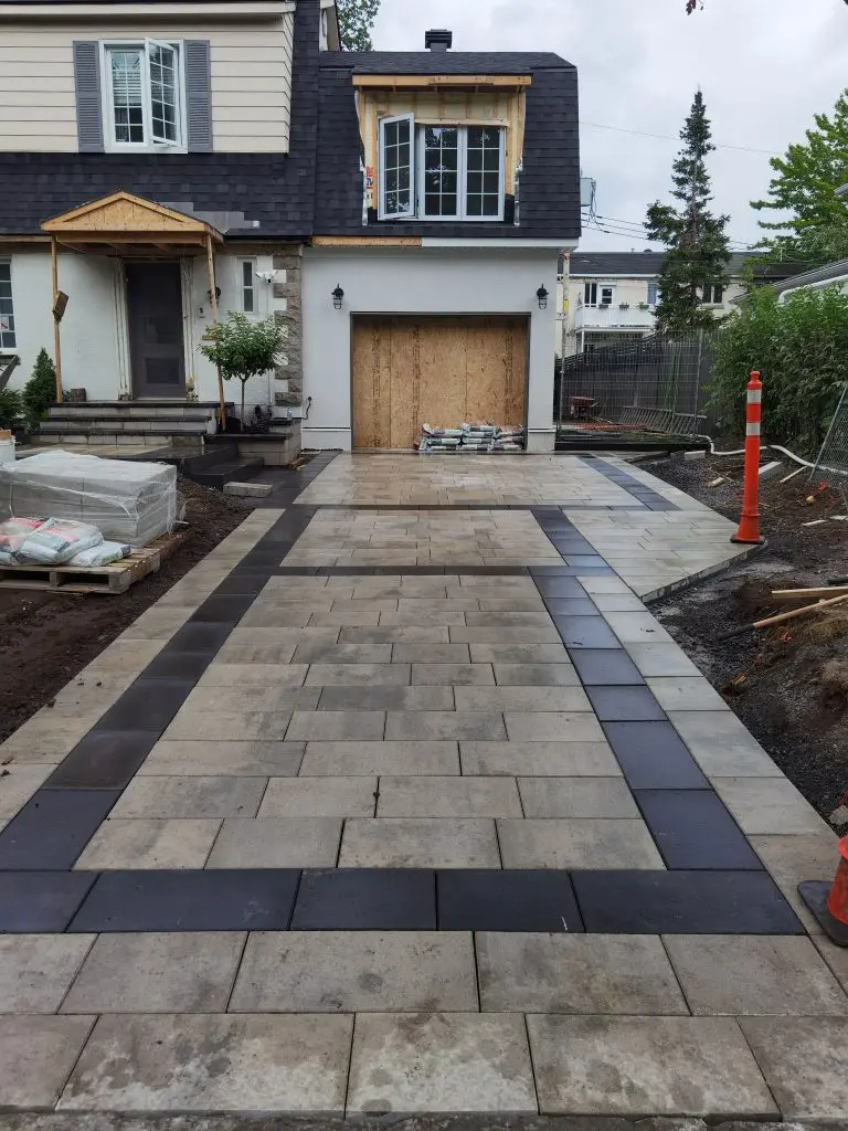 Residential interlocking paver driveway with black border, garage entrance and landscaping in progress