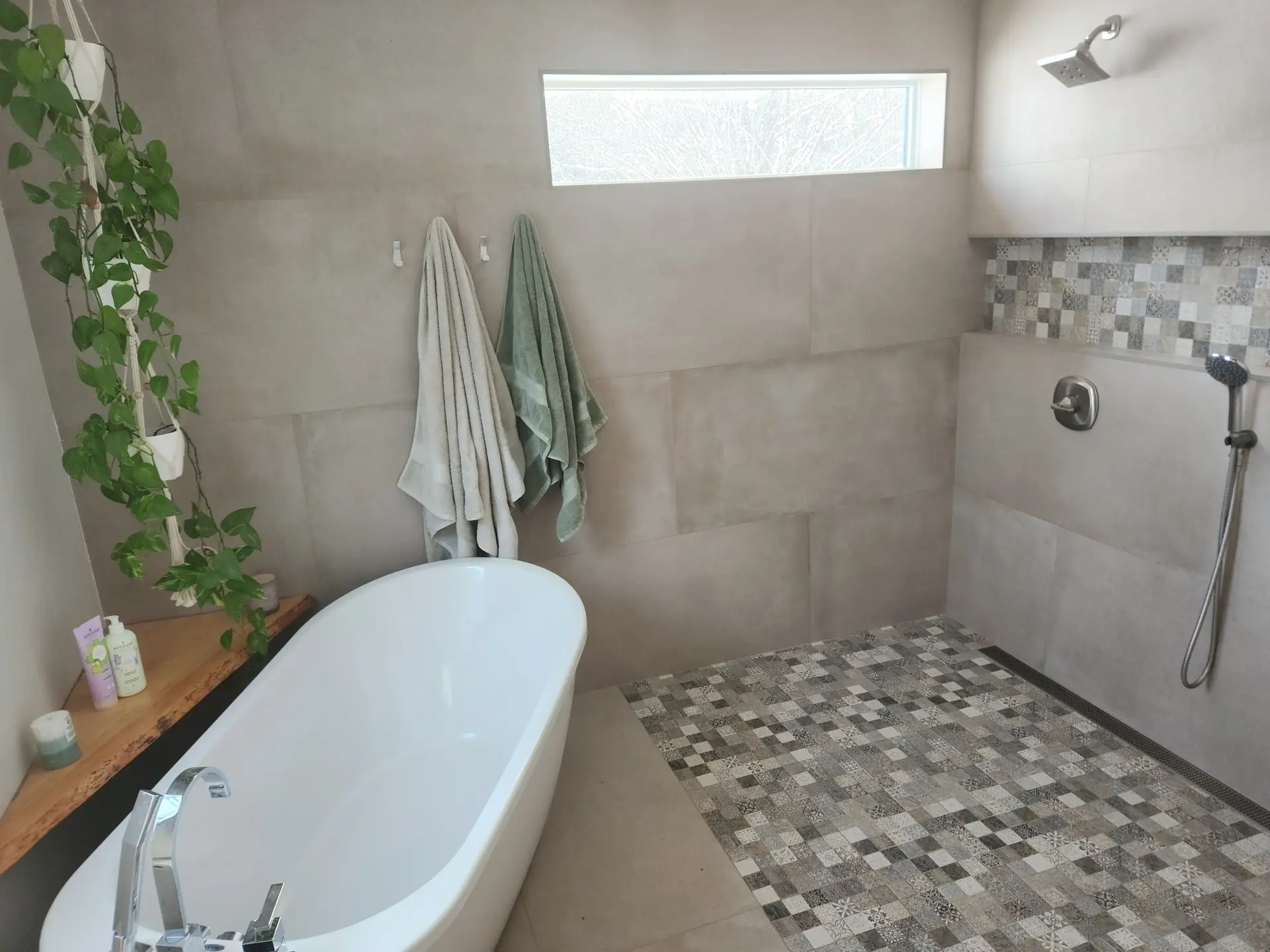 Modern bathroom with freestanding bathtub, walk-in shower, mosaic tile flooring, and natural plant decor.