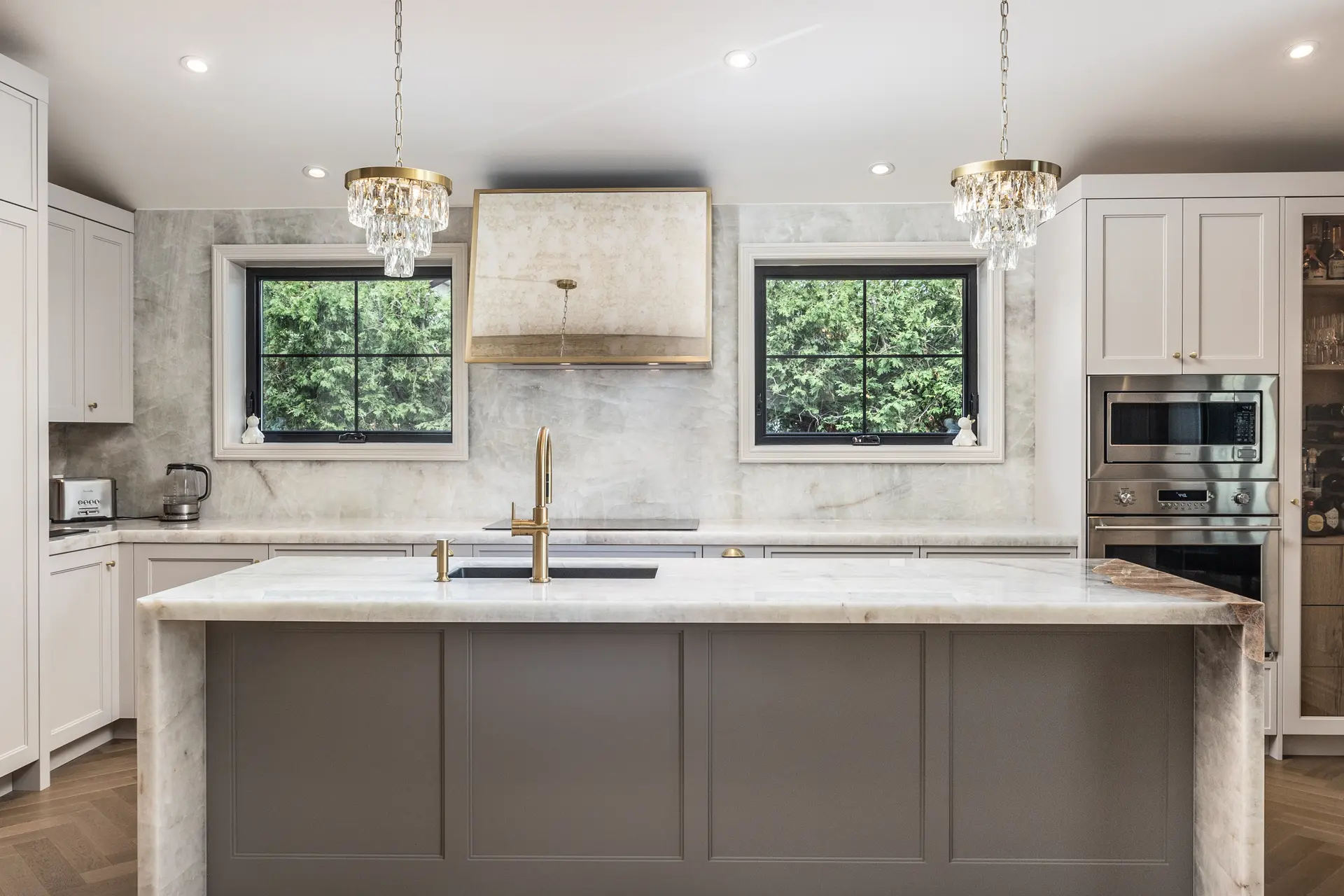 Cuisine haut de gamme avec grand îlot central, comptoirs en marbre veiné, électroménagers en inox et luminaires suspendus en verre.