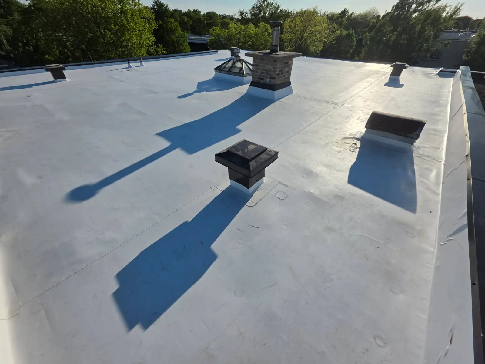 Toit plat blanc avec membrane étanche, cheminée en brique, évents de ventilation et puits de lumière sur bâtiment résidentiel