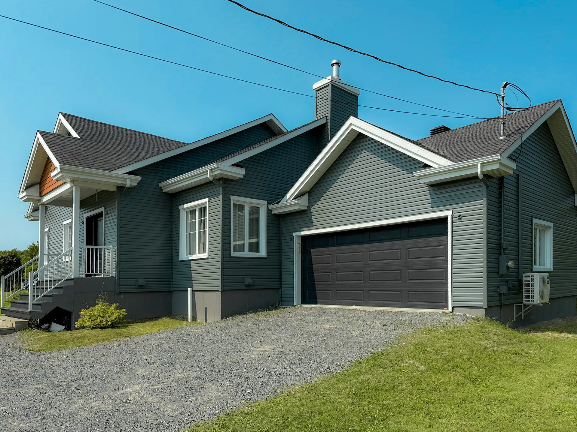 Modern single-family home with gray vinyl siding, a two-car garage, and black shingle roofing
