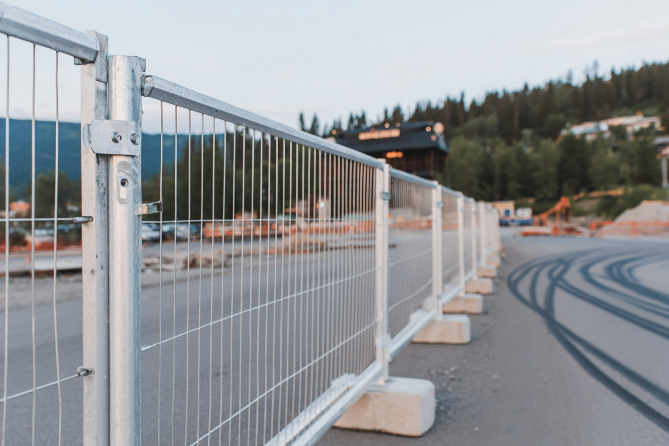 Metal security fence installed along a roadside on an outdoor construction site with mountains in background.