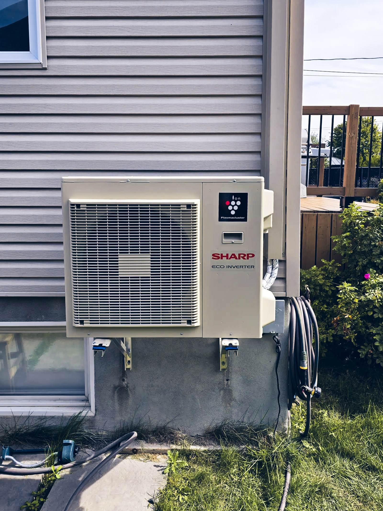 Sharp wall-mounted outdoor air conditioning unit installed on a vinyl-sided house wall
