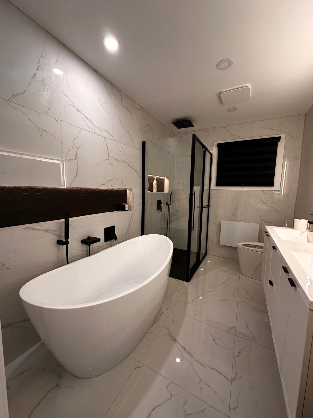 Salle de bain moderne en marbre avec baignoire autoportante, douche vitrée et robinetterie noire