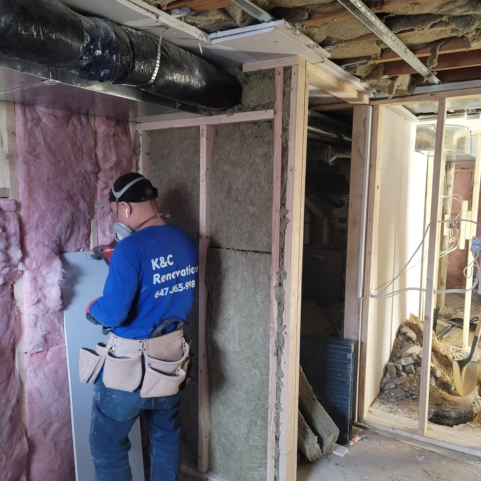 Renovation worker installing drywall panel with insulation and exposed wood framing in a basement