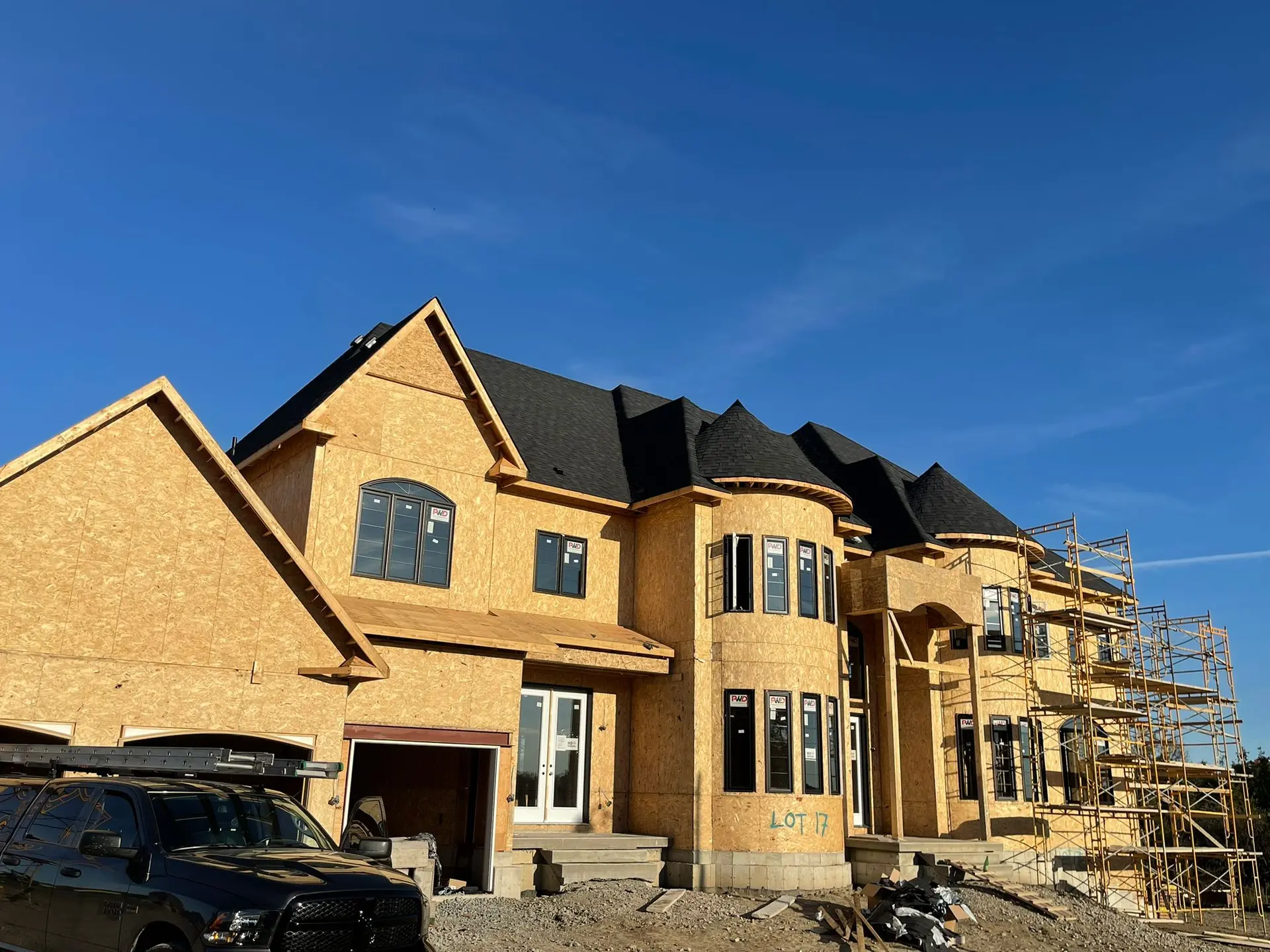 Construction d'une grande maison en bois avec toiture en bardeaux noirs et échafaudages sous un ciel bleu.