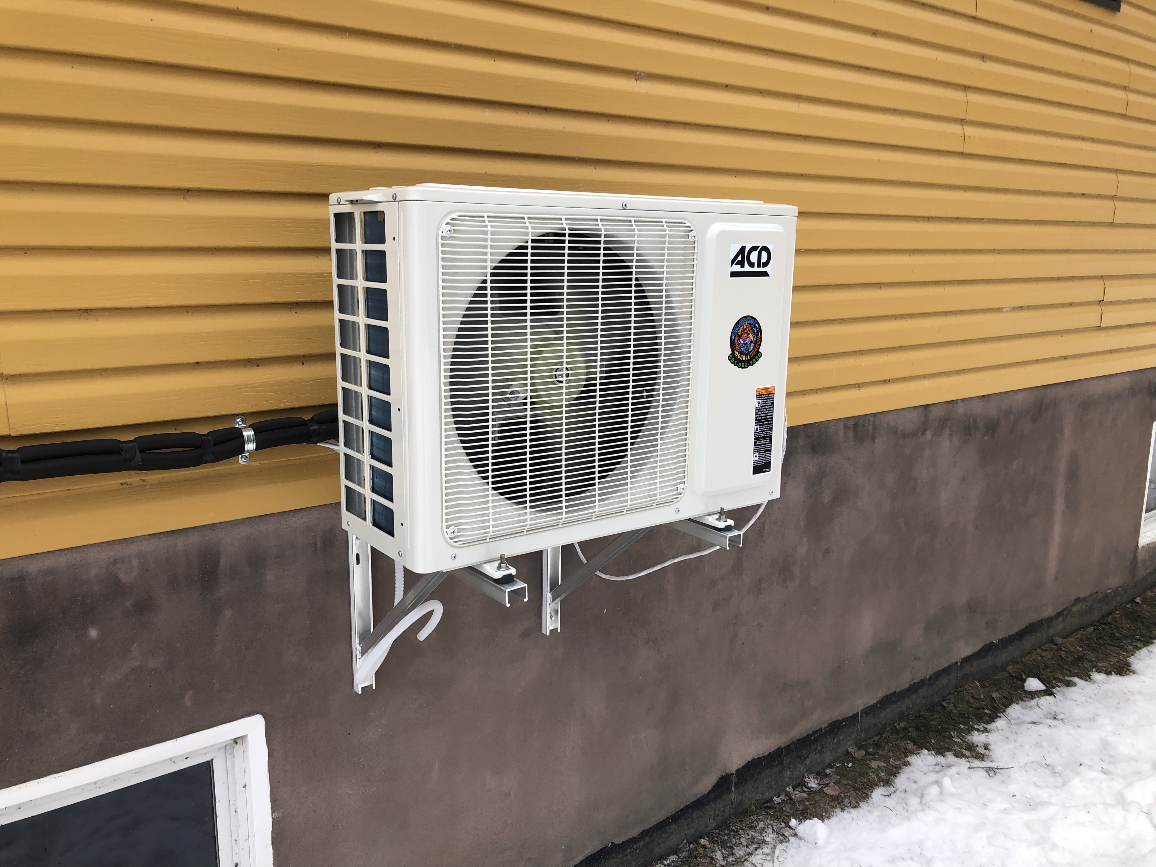 Outdoor air conditioning unit mounted on a yellow corrugated metal wall with metal wall brackets.