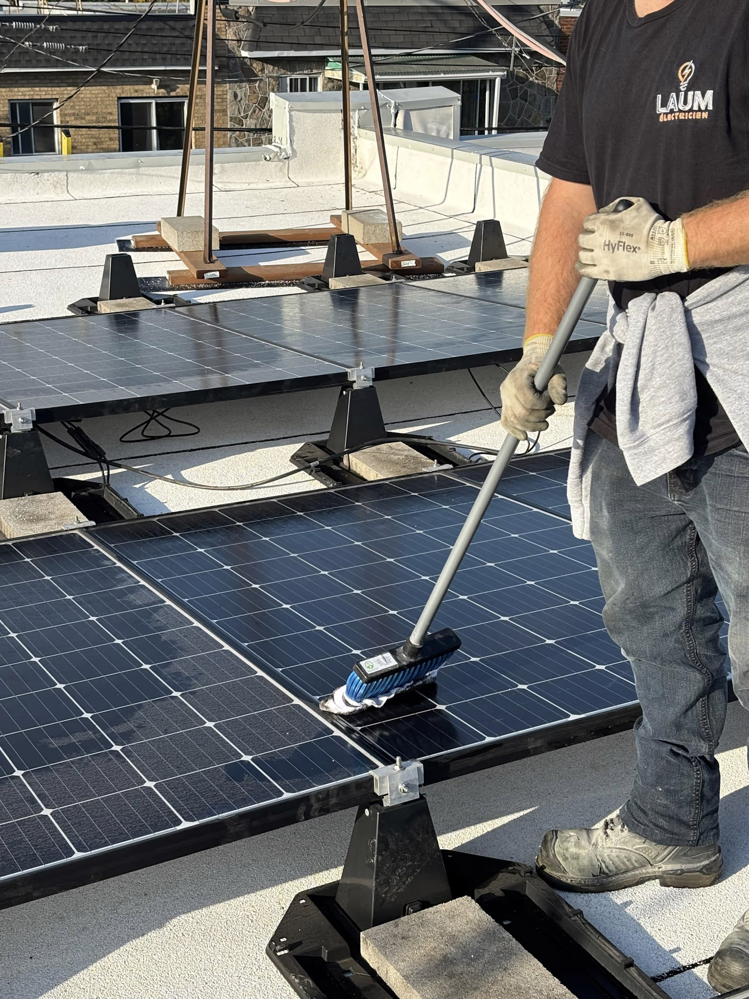 Electrician cleaning solar panels on a flat roof with brush, weighted mounts and white membrane