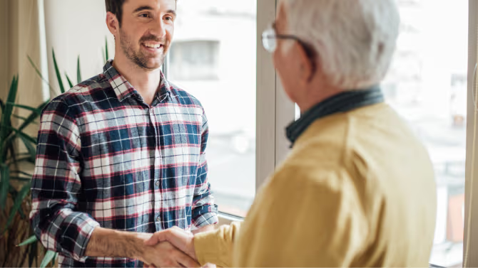 Rencontre professionnelle avec poignée de main entre un entrepreneur souriant et un client près d’une grande fenêtre.
