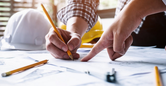Mains de professionnels annotant un plan architectural avec des crayons, avec des casques de construction sur une table de travail.