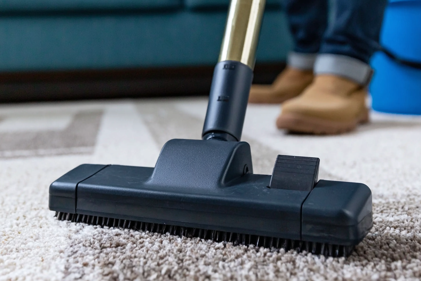 Close-up of a vacuum cleaner head cleaning a beige patterned rug in a living room