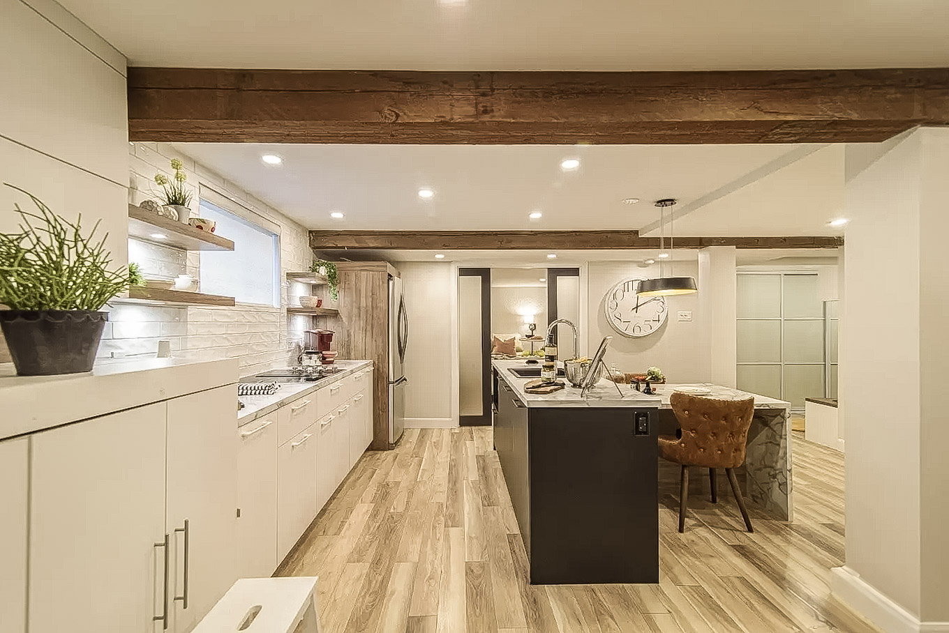Contemporary kitchen with exposed wooden beams, large black island, white cabinetry, and plant accents.