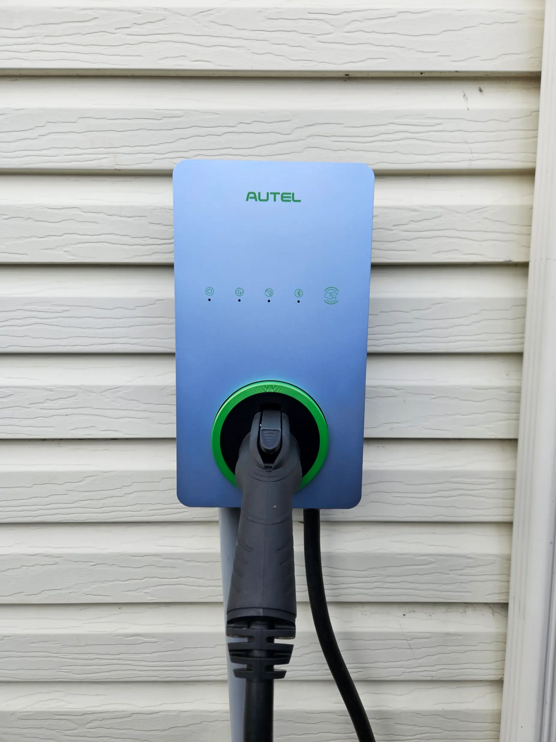 Borne de recharge Autel pour véhicule électrique installée sur un revêtement extérieur blanc avec connecteur branché et anneau lumineux vert