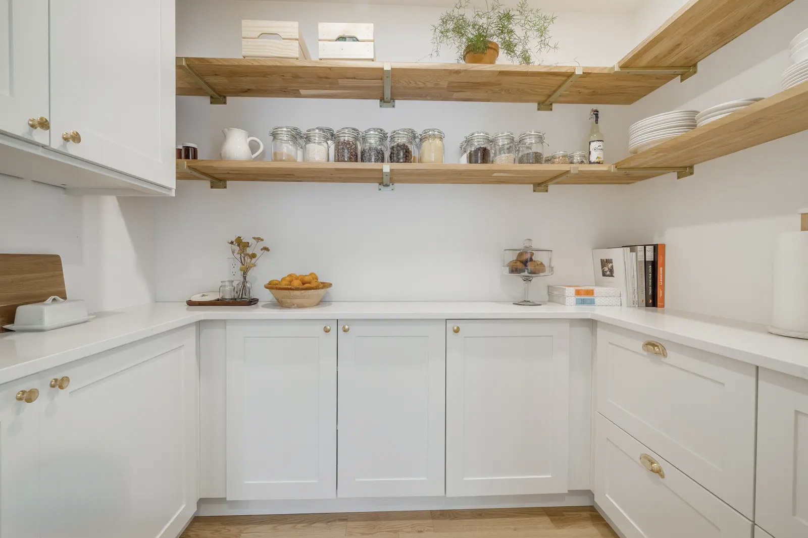 Garde-manger lumineux avec armoires blanches, comptoirs clairs, étagères ouvertes en bois et bocaux de rangement organisés.