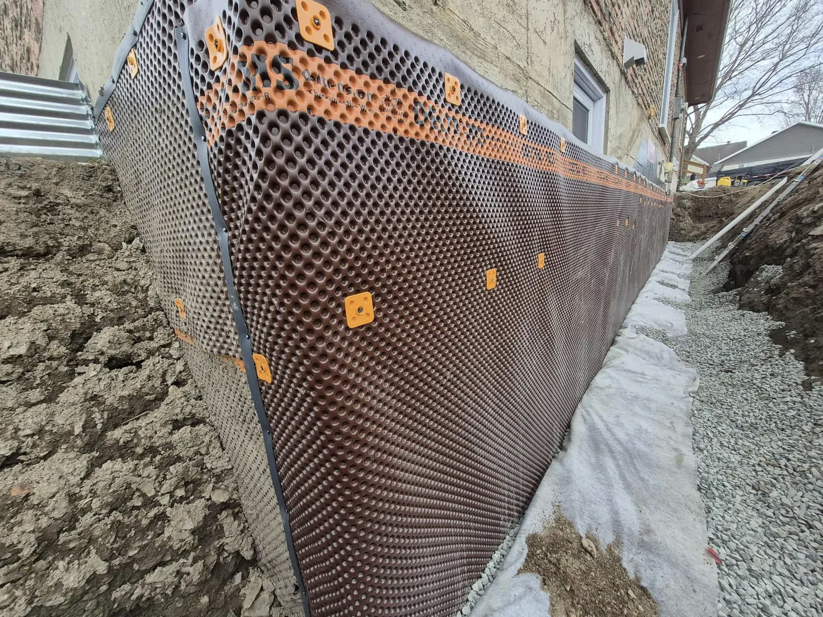 Installation of a dimpled waterproofing membrane on a house foundation during renovation to protect against moisture and water infiltration.