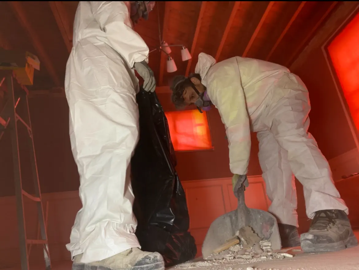 Techniciens en combinaison de protection retirant des débris dans un grenier lors d’une opération de décontamination