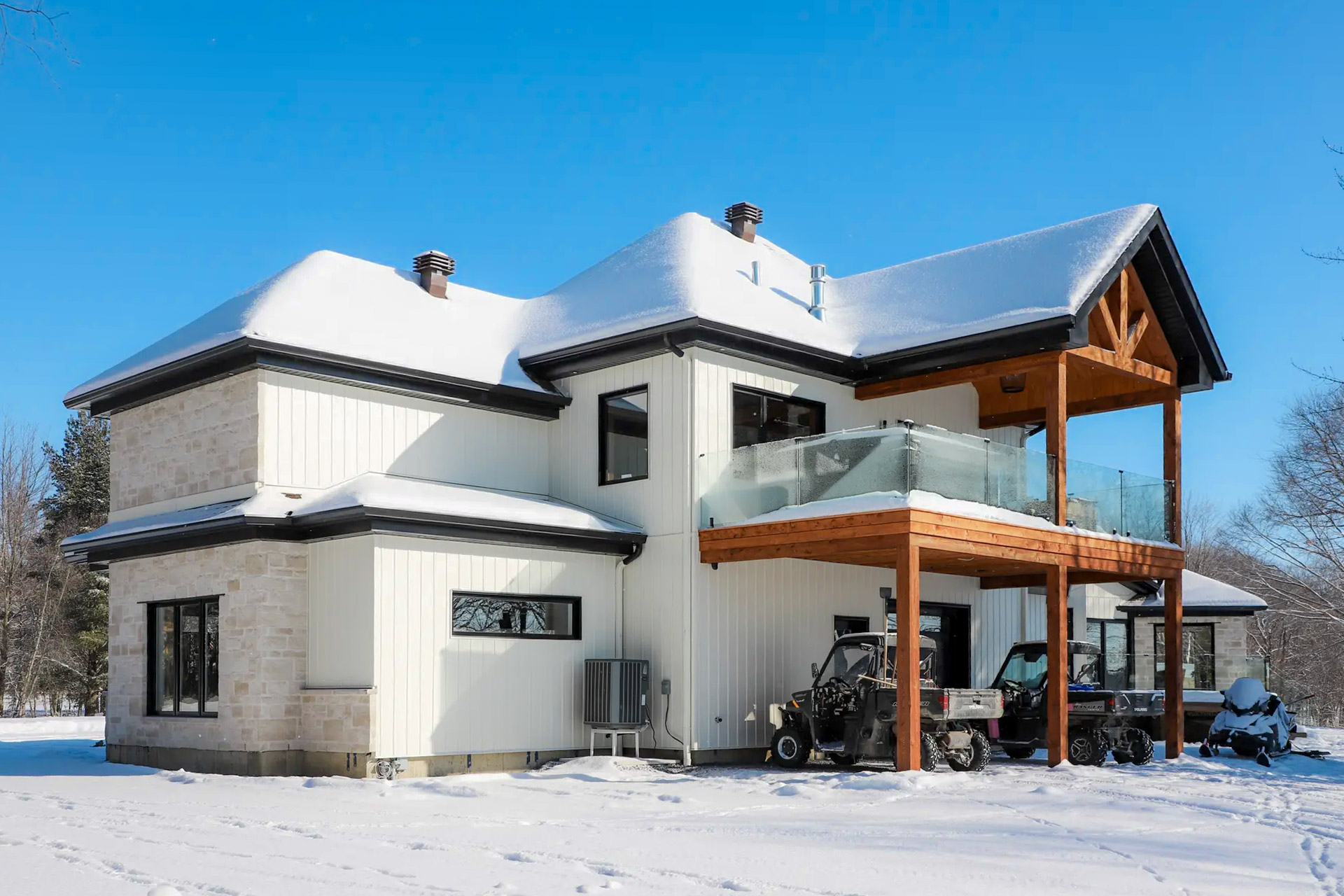 Modern house in winter with white exterior cladding, glass balcony, wooden beams and snow-covered roof