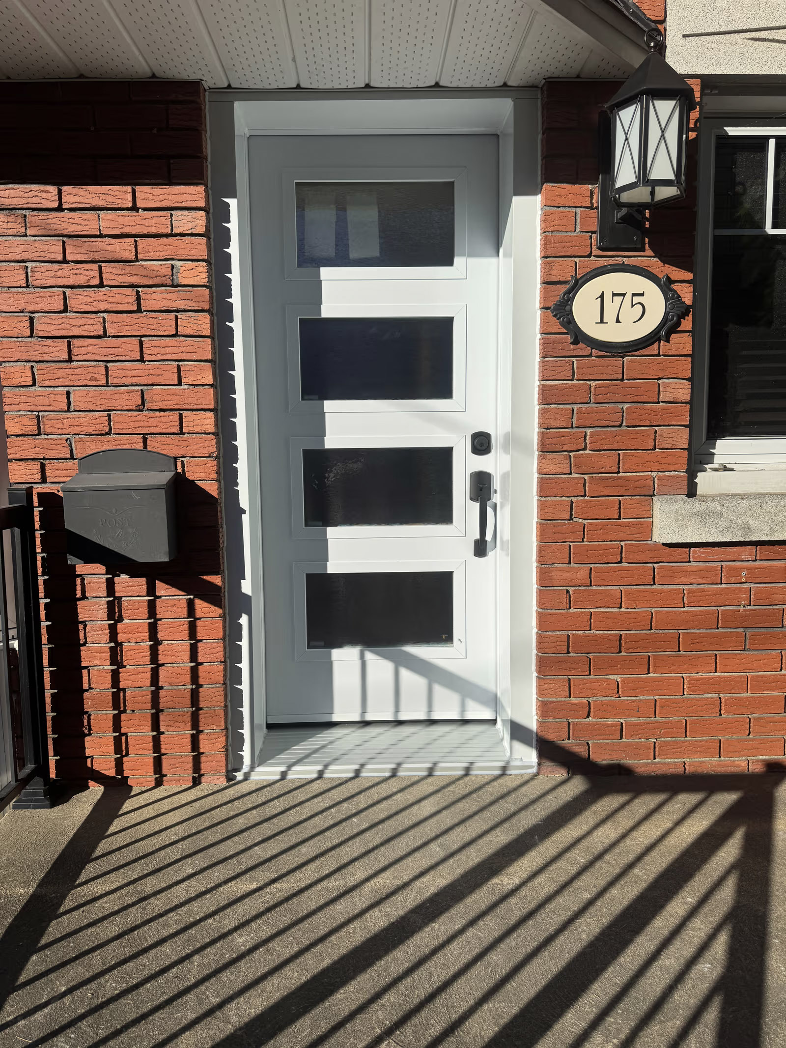 Porte d’entrée blanche moderne avec panneaux vitrés horizontaux sur façade en brique rouge
