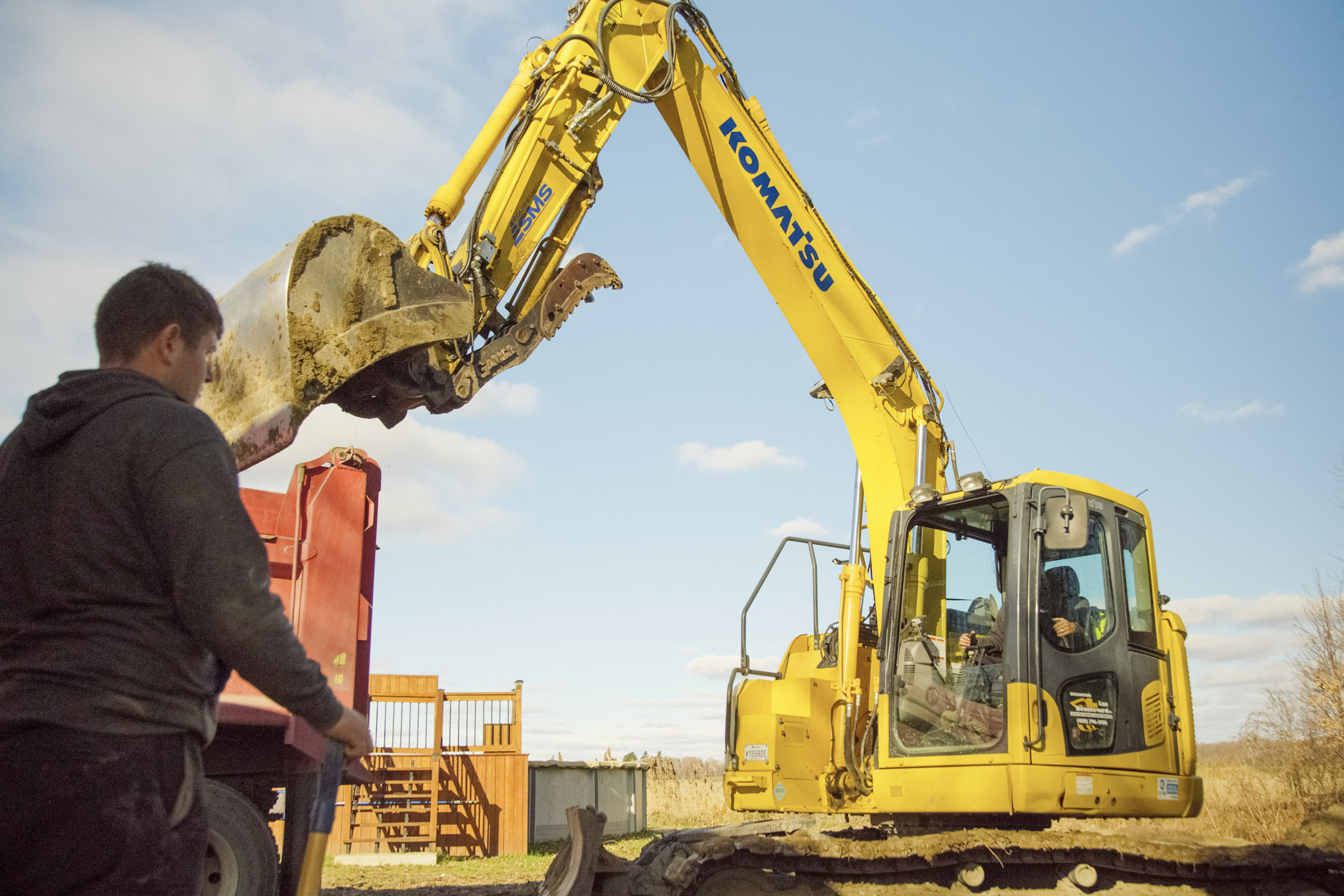 Soil loading operation with a Komatsu excavator and a red dump truck under the supervision of a worker