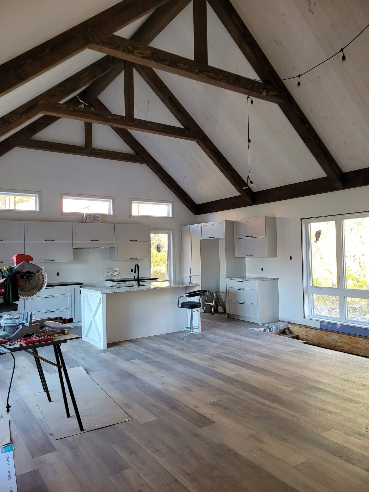Contemporary kitchen under renovation with vaulted ceiling, exposed wood beams, central island and wood-look flooring