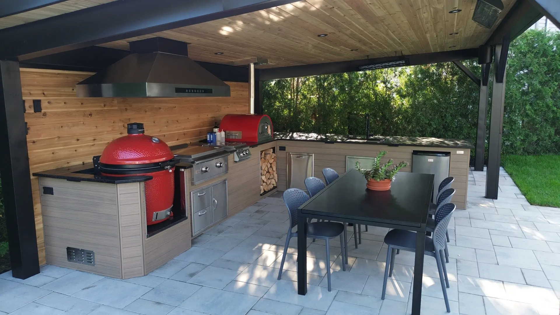 Cuisine extérieure moderne avec barbecue en céramique rouge, four à pizza, comptoirs en bois et coin repas couvert