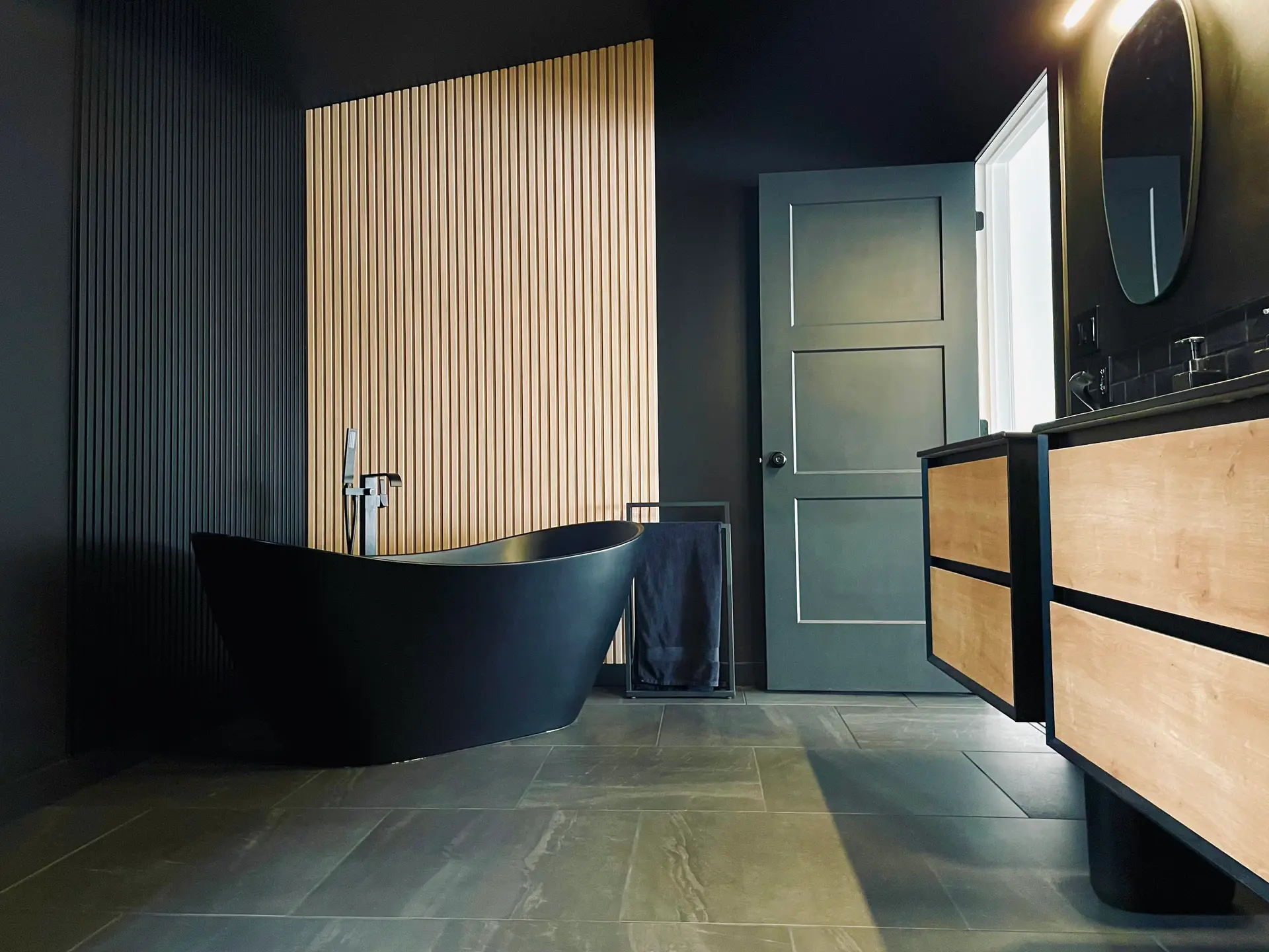 Salle de bain contemporaine sombre avec baignoire autoportante noire, meuble en bois et mur à lattes décoratif