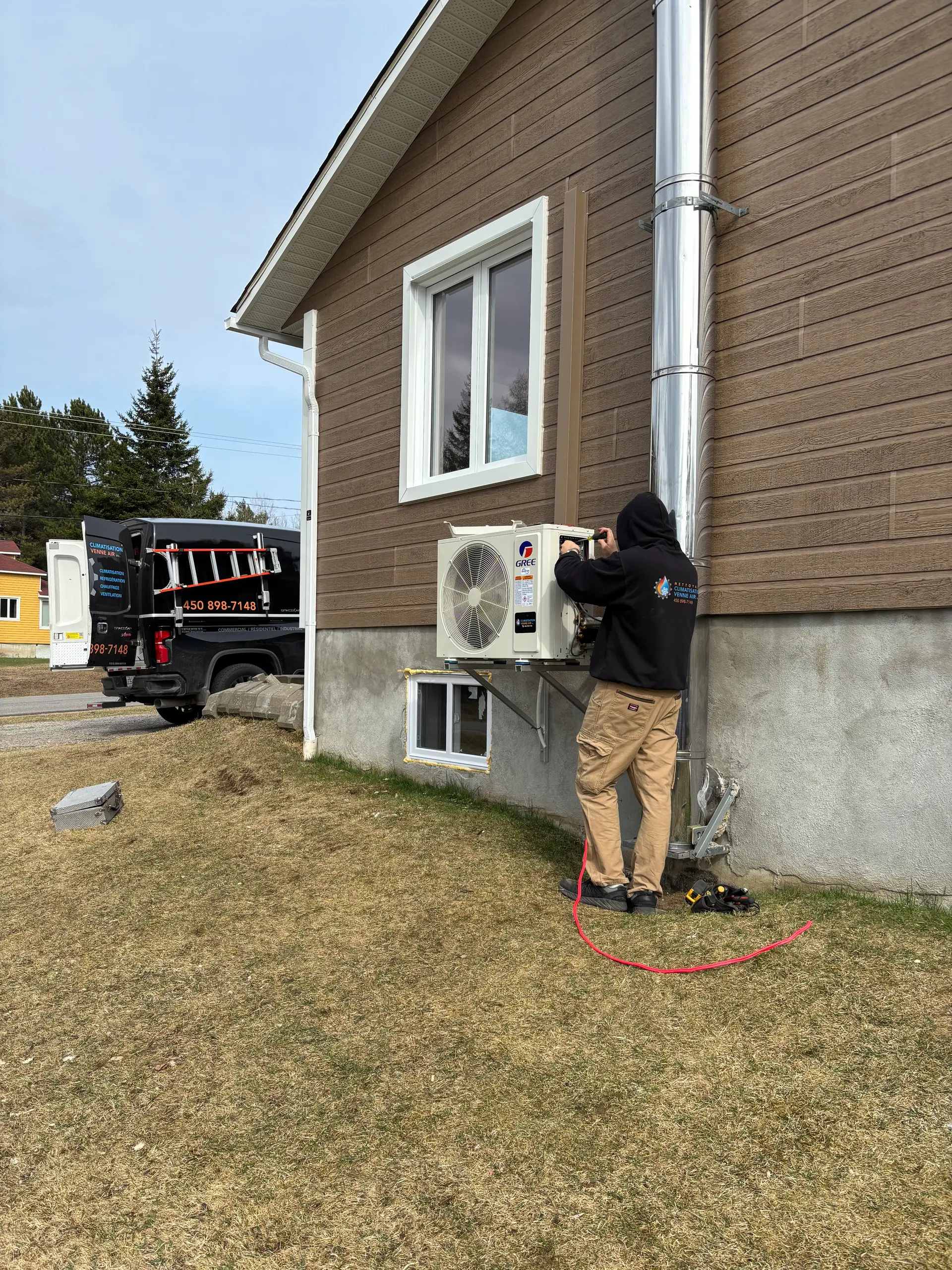 Technicien en train d’installer ou d’entretenir une unité de climatisation murale sur la façade extérieure d’une maison résidentielle