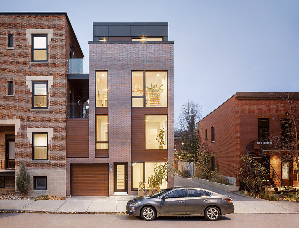 Modern facade of a brick and wood townhouse with large windows and integrated garage