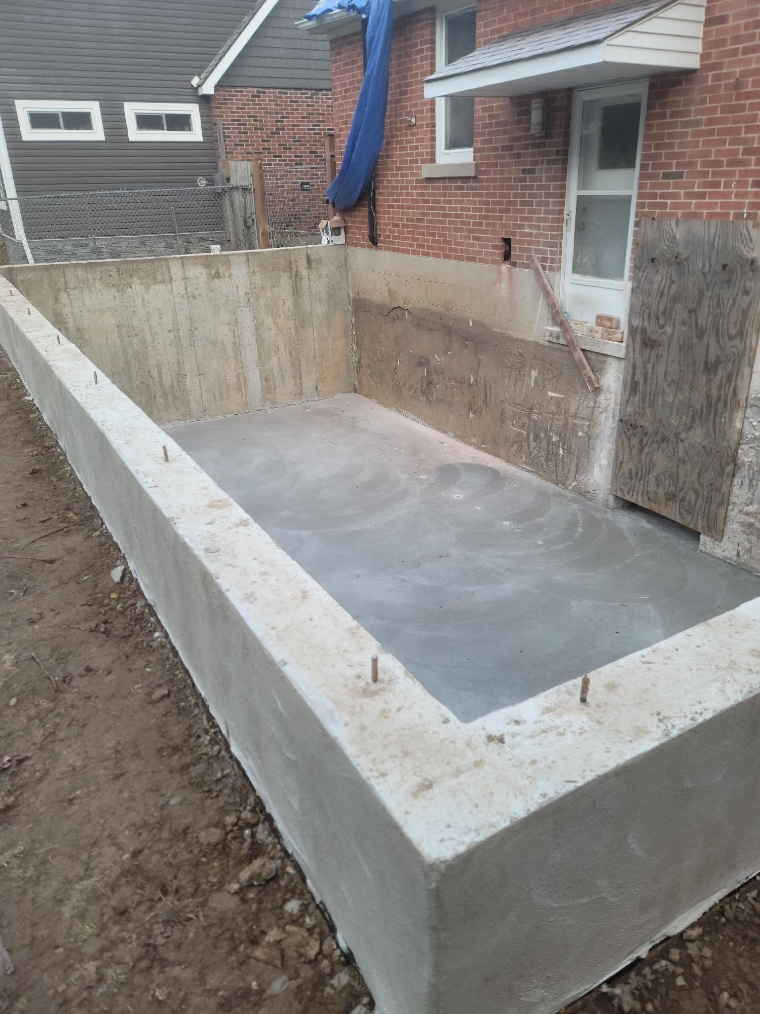 Nouvelle fondation en béton coulée pour agrandissement de maison à l’arrière d’un bâtiment en brique, en cours de construction.