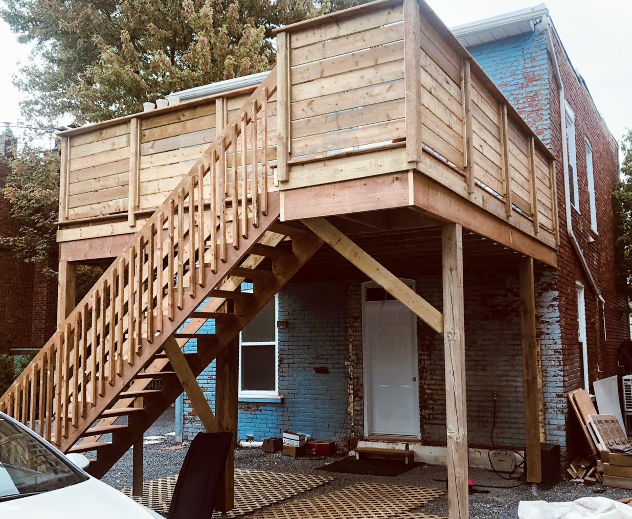 Terrasse en bois surélevée avec escalier, garde-corps et structure de soutien adossée à une maison en brique