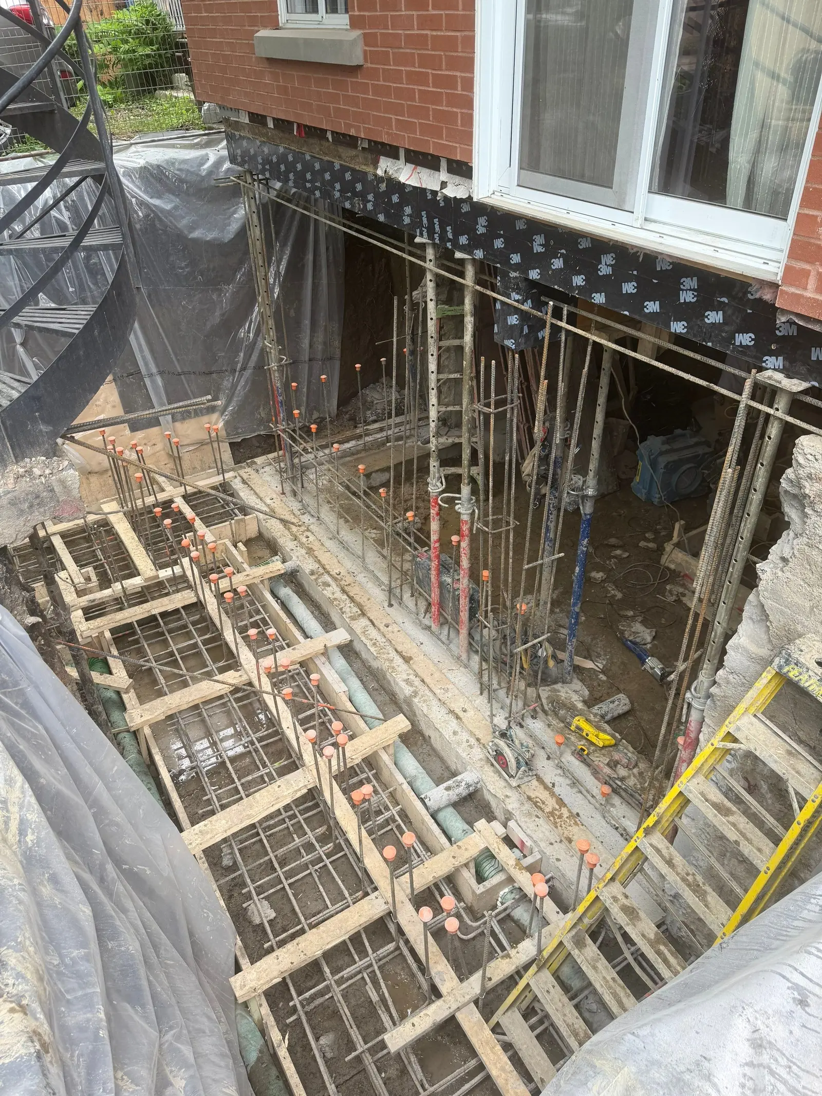 Excavated foundation work under a brick house with formwork, steel rebar, shoring, drain and waterproofing