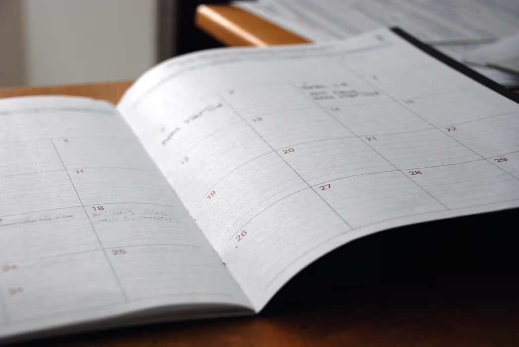 Open paper planner on a table with monthly calendar, visible dates and blurred handwritten notes.