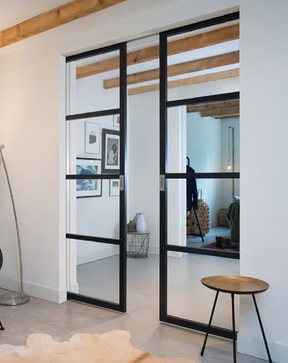 Portes coulissantes vitrées au cadre noir dans un intérieur lumineux avec poutres en bois apparentes et style contemporain.